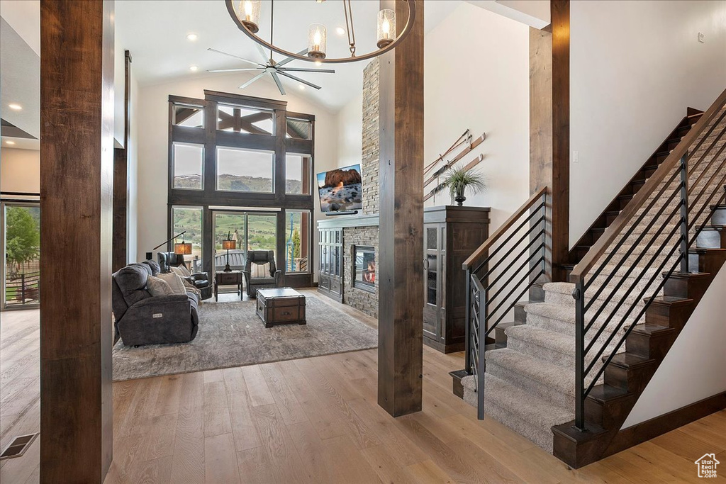 Living area featuring hardwood / wood-style floors, a stone fireplace, stairway, a chandelier, and high vaulted ceiling