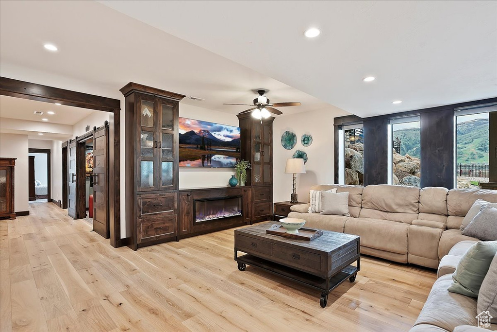 Living area featuring a barn door, recessed lighting, light wood finished floors, a glass covered fireplace, and a ceiling fan