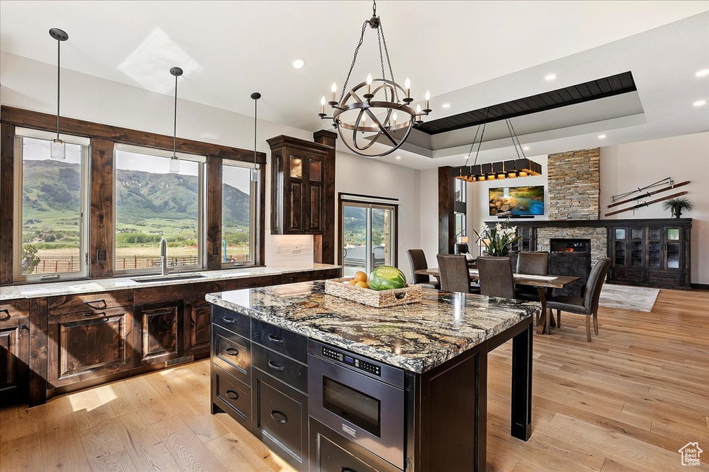 Kitchen with a sink, a raised ceiling, light wood-style floors, a chandelier, and pendant lighting