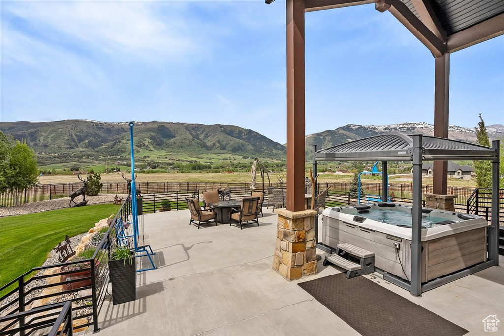 View of patio featuring a hot tub, a mountain view, fence, a fire pit, and a gazebo