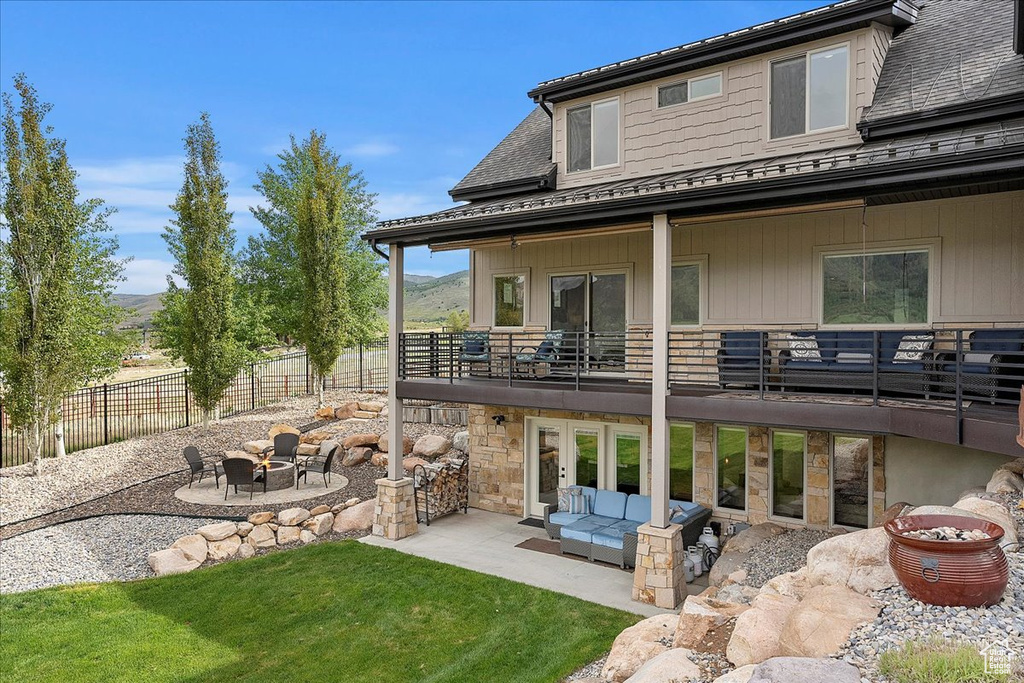 Rear view of house with a patio, a balcony, an outdoor living space with a fire pit, stone siding, and a shingled roof