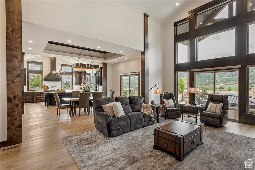 Living room featuring healthy amount of natural light, light wood-style flooring, a towering ceiling, recessed lighting, and a tray ceiling
