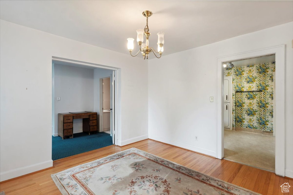 Empty room with a chandelier, wood finished floors, and baseboards