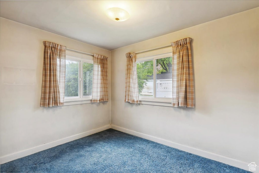 Unfurnished room with healthy amount of natural light, dark colored carpet, and baseboards