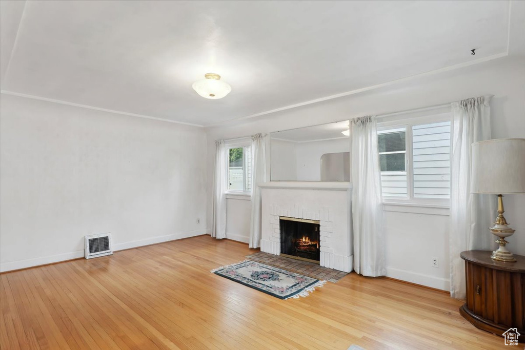 Unfurnished living room featuring wood finished floors, a brick fireplace, and baseboards