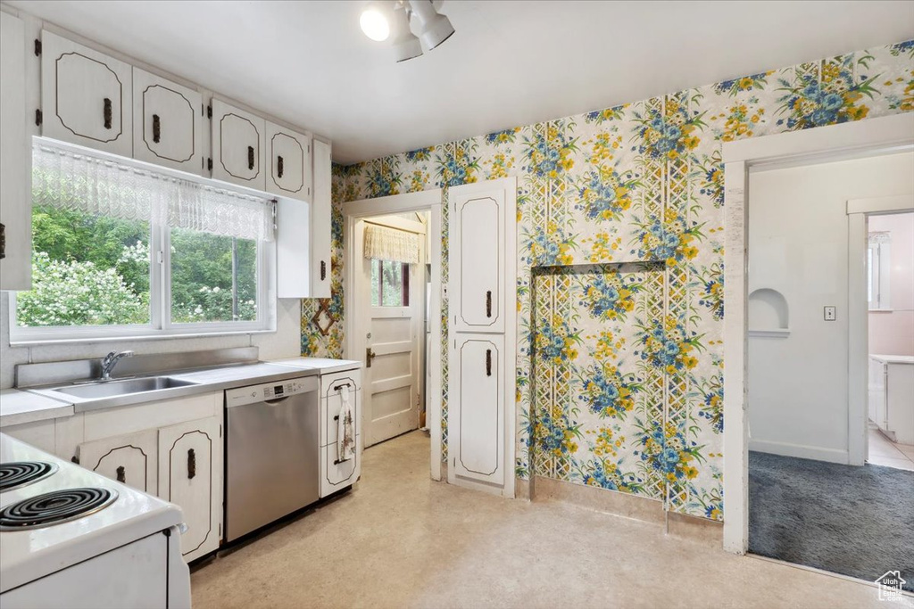 Kitchen with stainless steel dishwasher, a sink, wallpapered walls, light countertops, and white cabinets