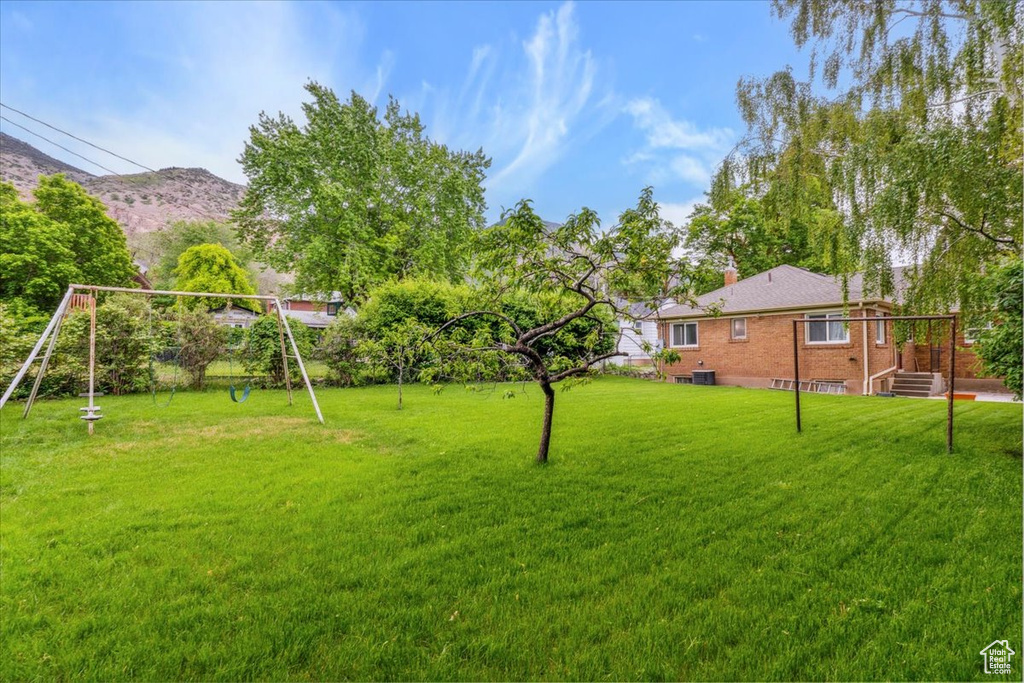 View of grassy yard featuring a playground and a mountain view