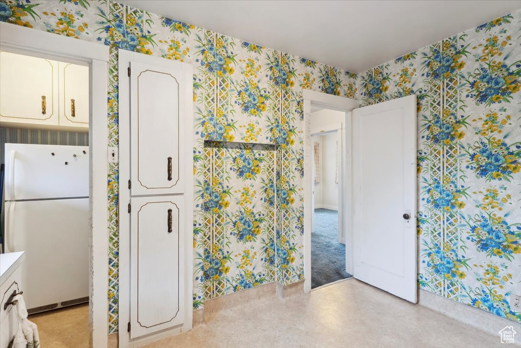 Kitchen featuring freestanding refrigerator, wallpapered walls, white cabinetry, and light countertops