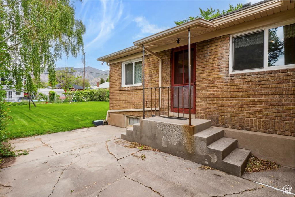 View of exterior entry featuring a yard, brick siding, a patio area, and a mountain view