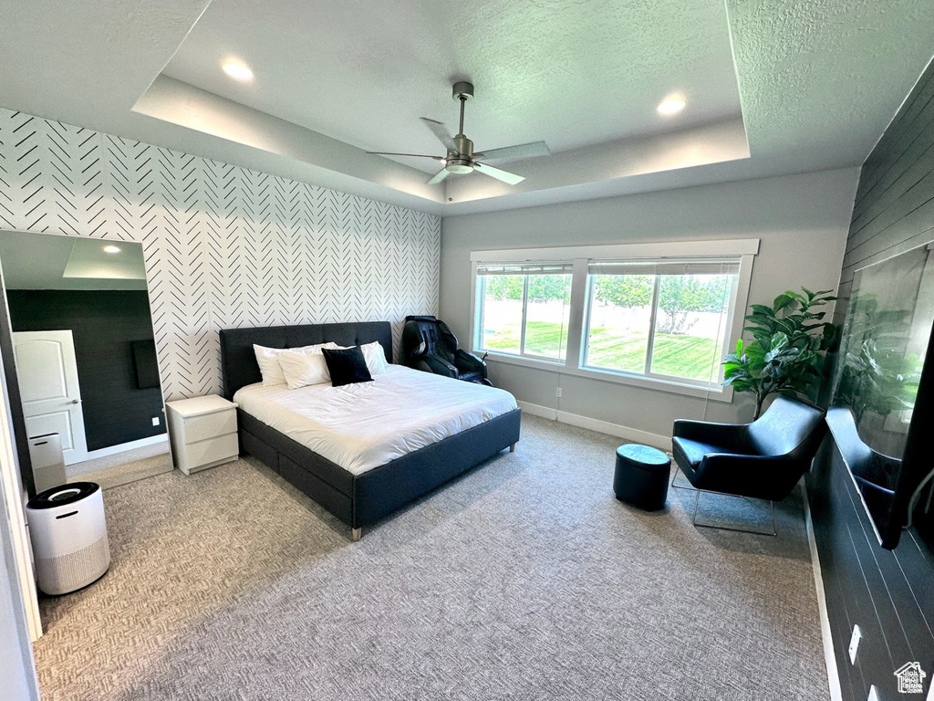 Carpeted bedroom with an accent wall, wallpapered walls, baseboards, a tray ceiling, and a textured ceiling