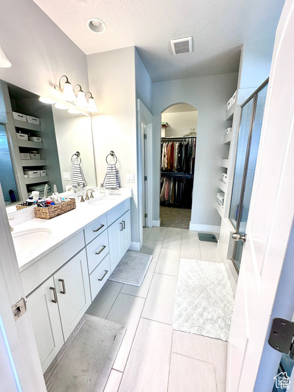Full bathroom featuring a stall shower, double vanity, a walk in closet, a textured ceiling, and baseboards