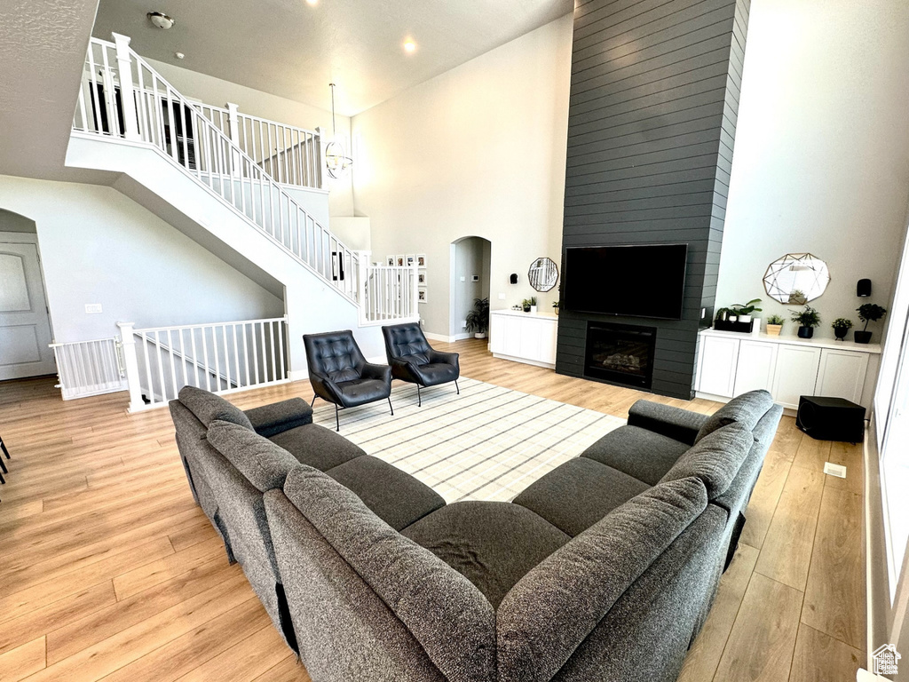 Living room with a towering ceiling, arched walkways, wood finished floors, a fireplace, and recessed lighting