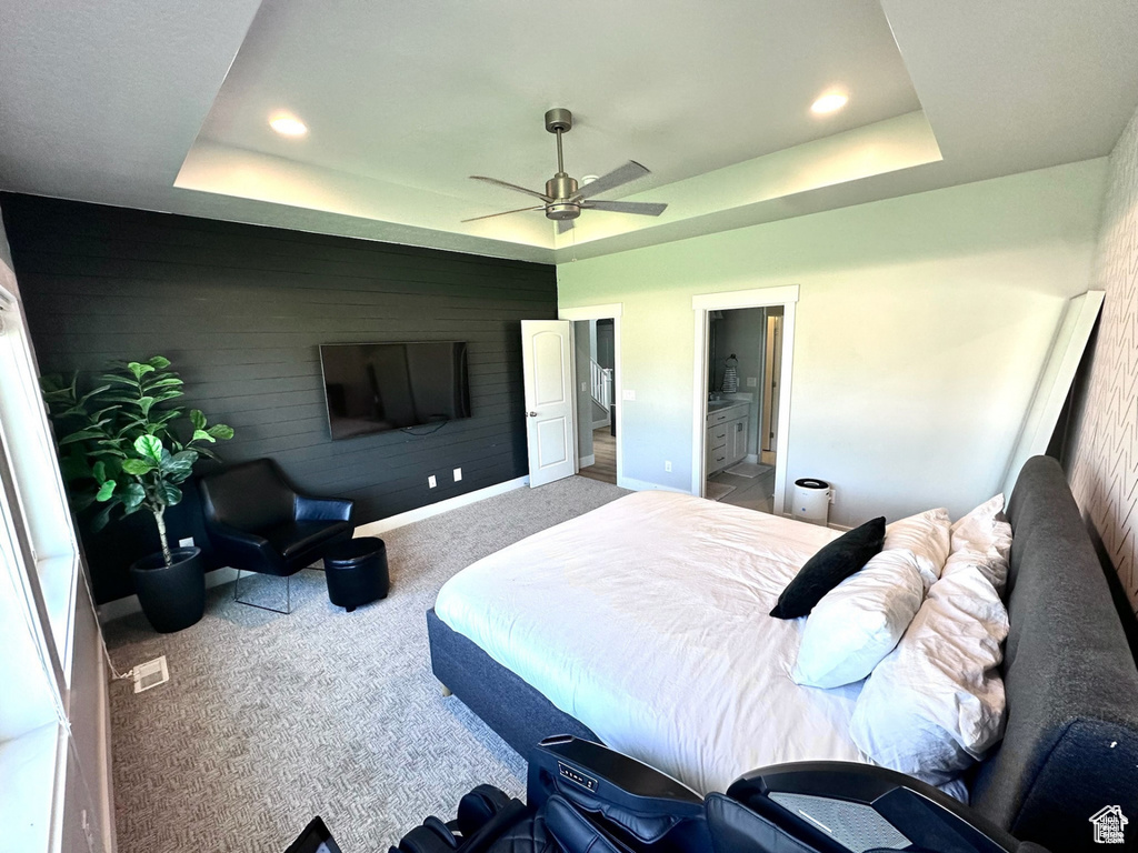 Carpeted bedroom featuring a raised ceiling, baseboards, recessed lighting, ceiling fan, and ensuite bathroom