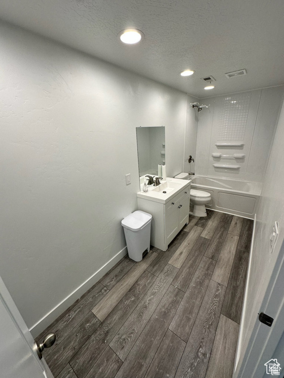 Bathroom featuring toilet, wood finished floors,  shower combination, vanity, and a textured ceiling