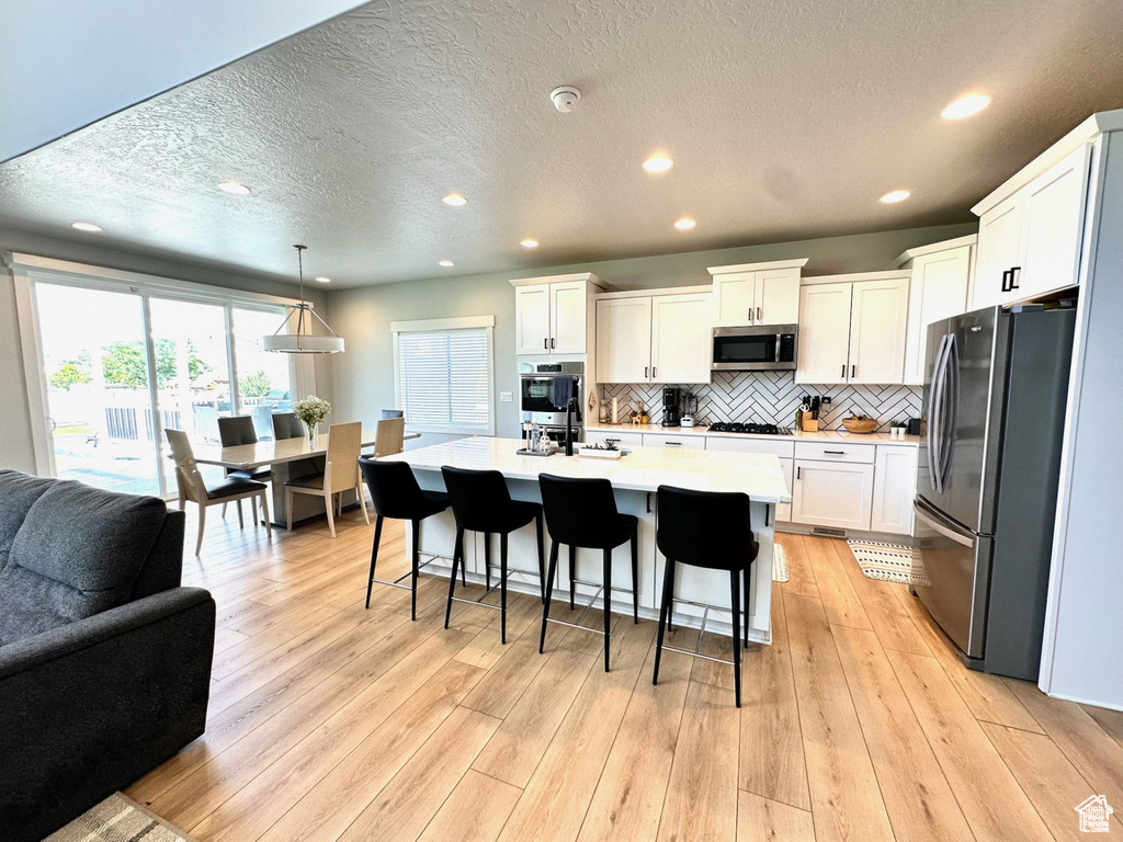 Kitchen featuring stainless steel appliances, open floor plan, light countertops, recessed lighting, and a kitchen breakfast bar