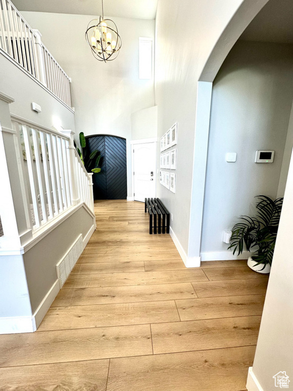 Entryway with wood finished floors, arched walkways, a towering ceiling, baseboards, and a chandelier