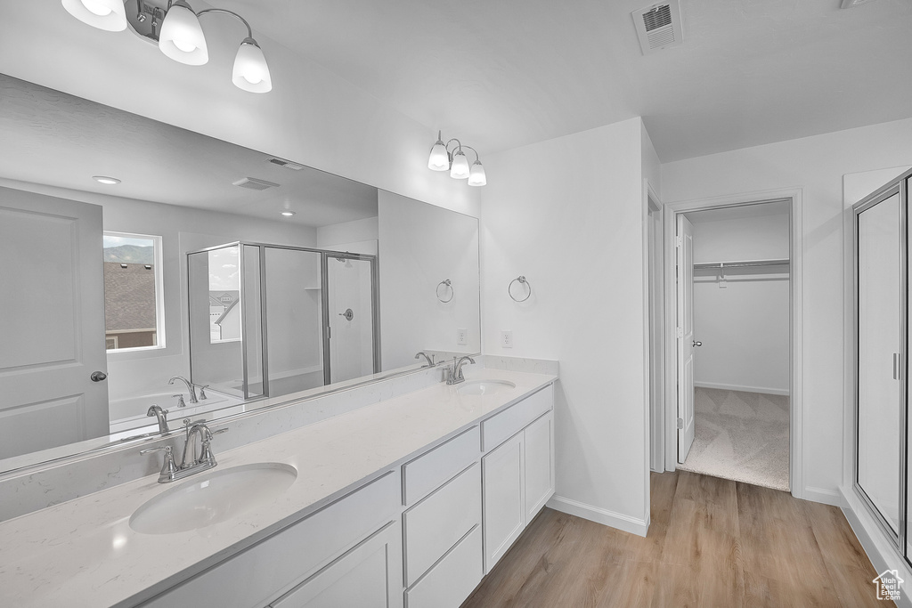 Full bathroom with a shower stall, a walk in closet, wood finished floors, double vanity, and a garden tub