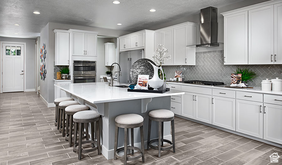 Kitchen featuring wall chimney range hood, stainless steel appliances, wood tiled floors, a kitchen breakfast bar, and recessed lighting