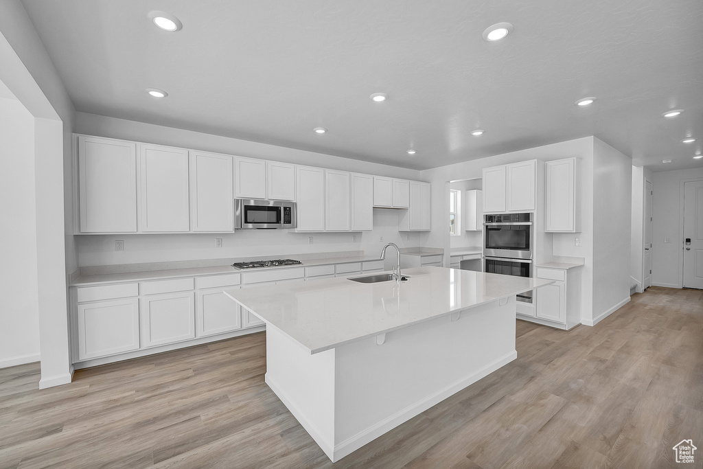 Kitchen featuring appliances with stainless steel finishes, a sink, recessed lighting, an island with sink, and white cabinetry