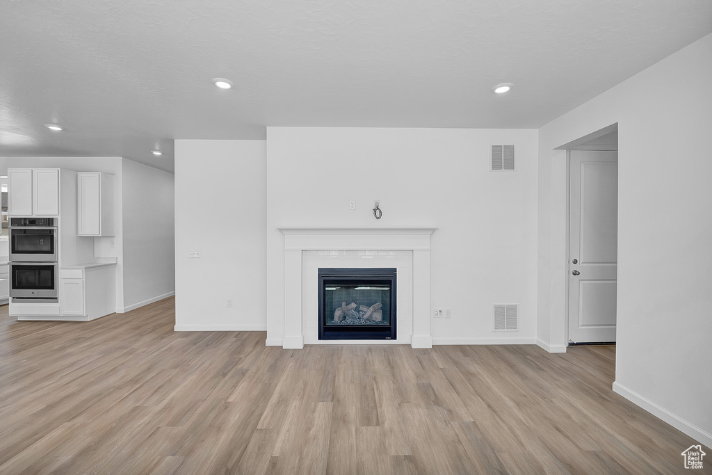 Unfurnished living room with light wood-style flooring, baseboards, a glass covered fireplace, and recessed lighting