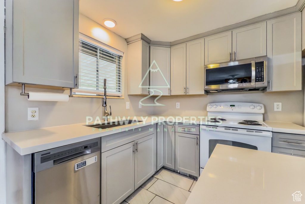 Kitchen with appliances with stainless steel finishes, gray cabinets, light countertops, and a sink