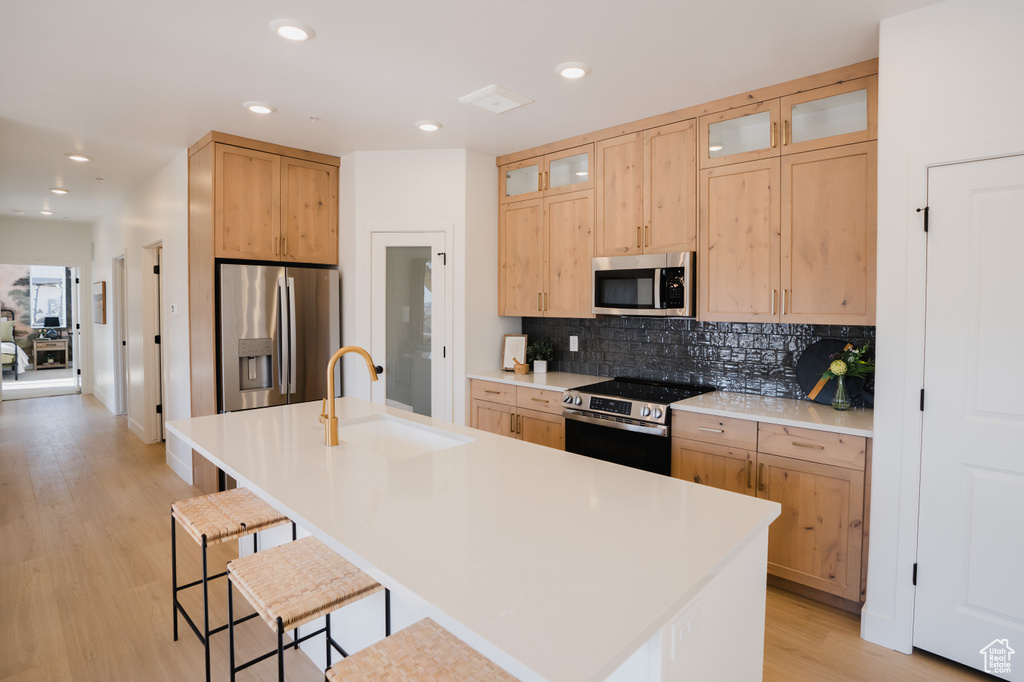 Kitchen featuring stainless steel appliances, a sink, light brown cabinets, a kitchen breakfast bar, and backsplash