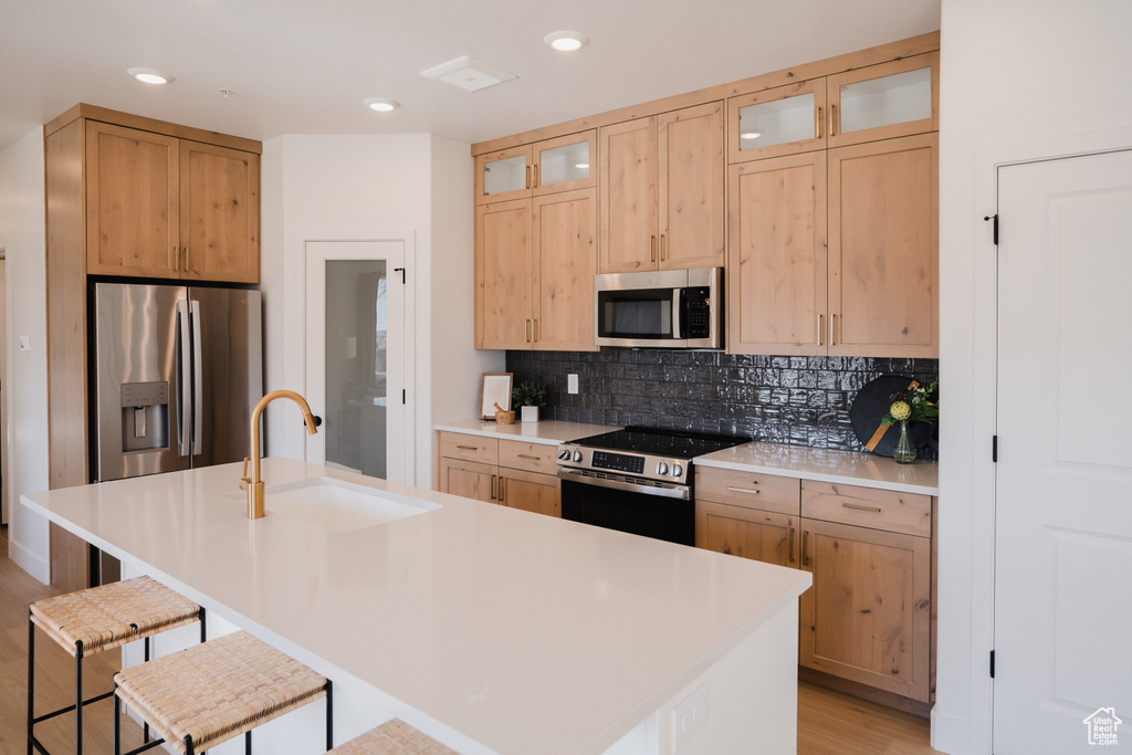 Kitchen with a sink, stainless steel appliances, a kitchen bar, glass insert cabinets, and decorative backsplash