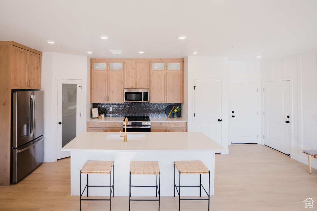 Kitchen featuring appliances with stainless steel finishes, light wood finished floors, a sink, a breakfast bar area, and recessed lighting