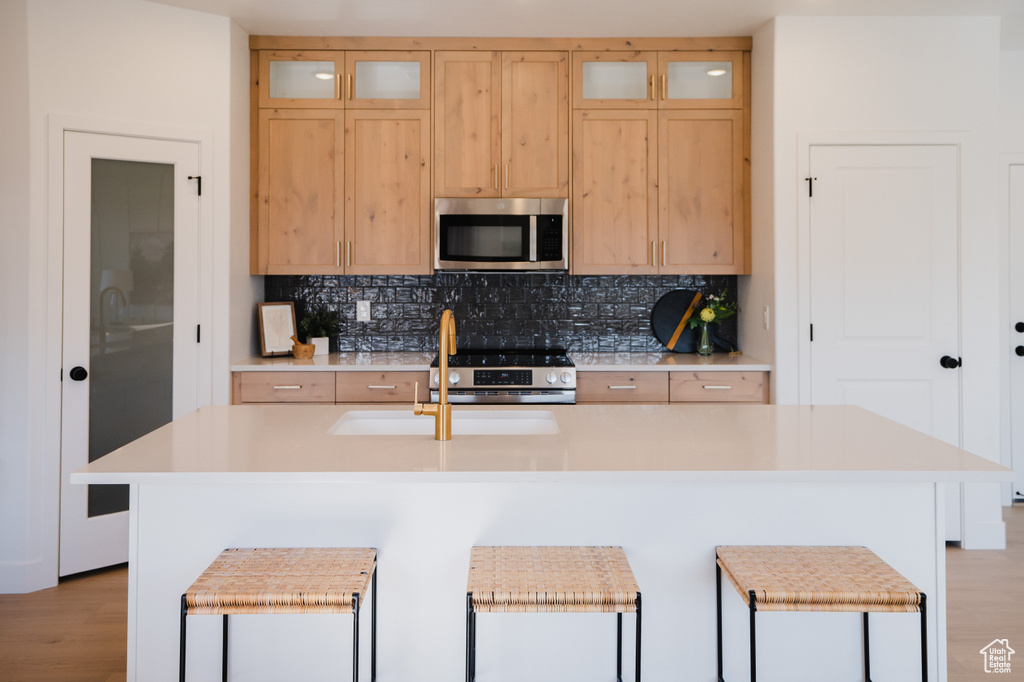 Kitchen featuring appliances with stainless steel finishes, light countertops, backsplash, a center island with sink, and light brown cabinetry