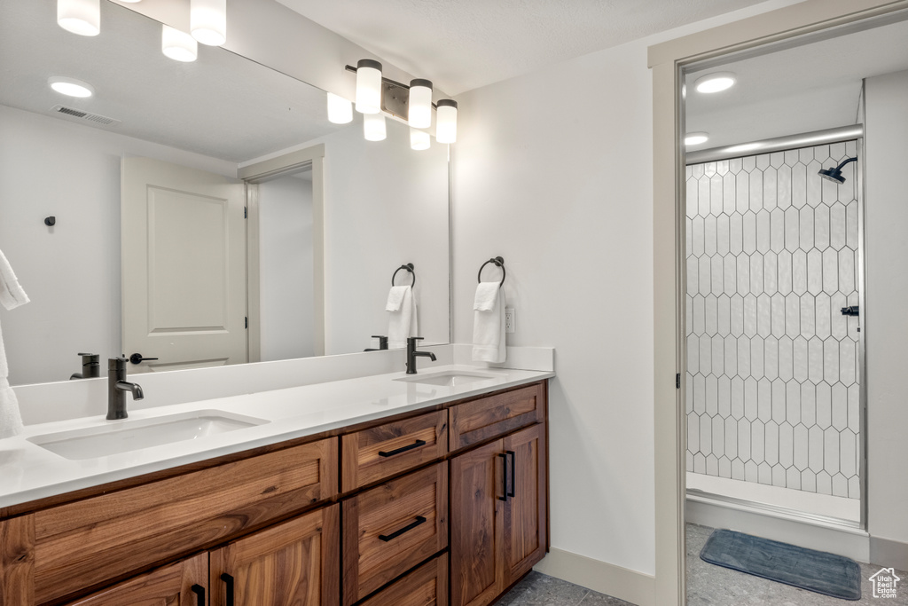 Full bathroom featuring a tile shower, double vanity, baseboards, and recessed lighting