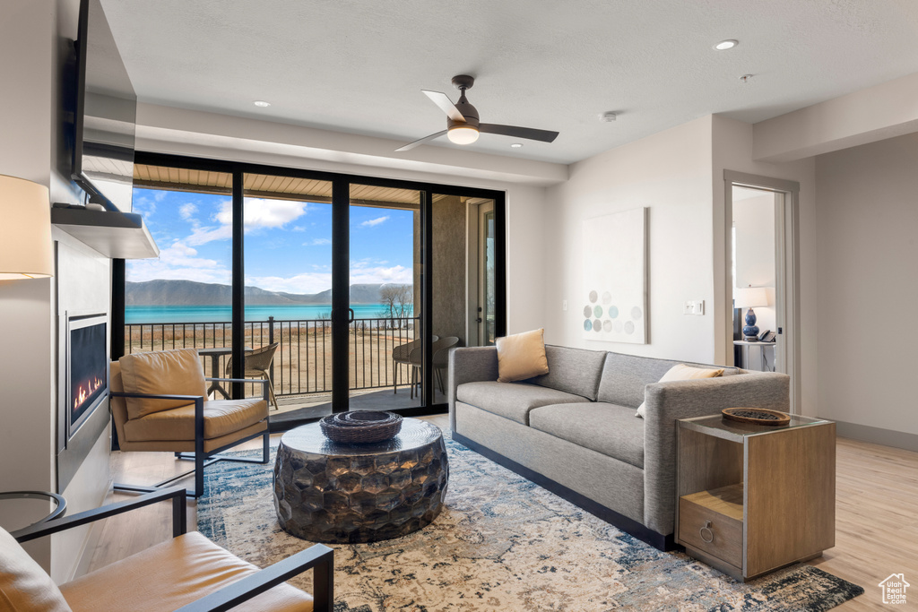 Living room featuring a ceiling fan, wood finished floors, a lit fireplace, recessed lighting, and a water view