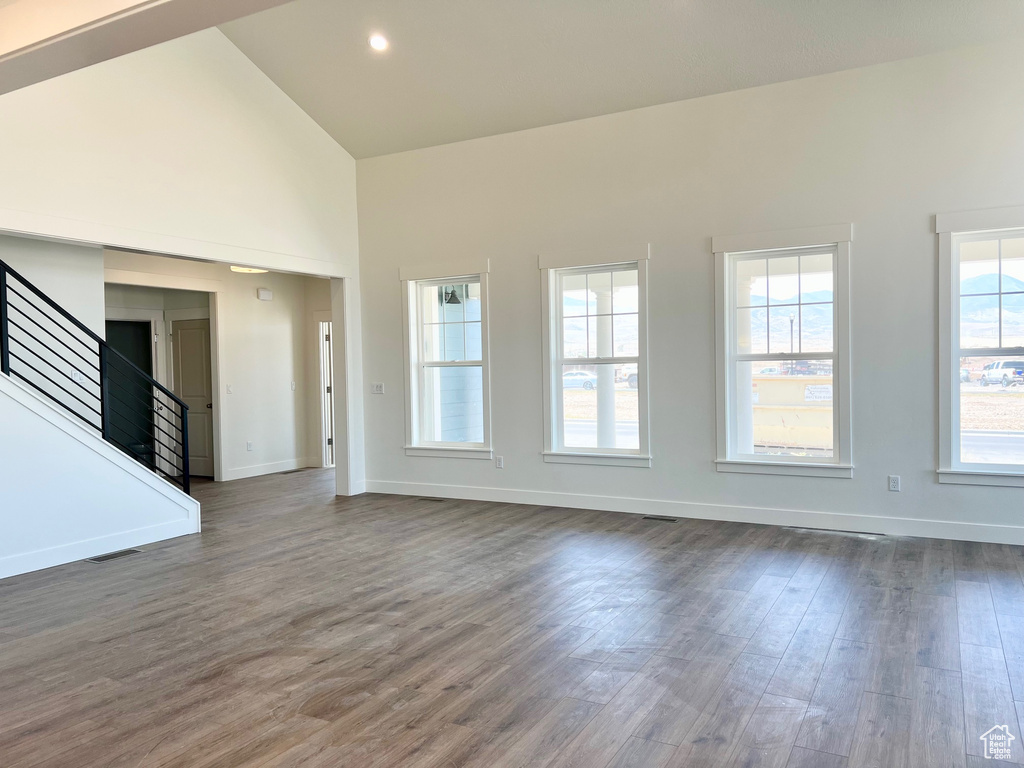 Unfurnished living room with high vaulted ceiling, stairway, and dark wood-style flooring