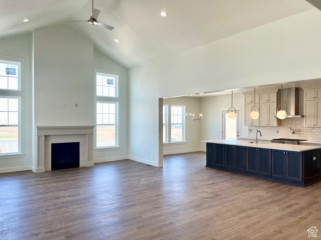 Kitchen with wall chimney exhaust hood, high vaulted ceiling, light countertops, a kitchen island with sink, and a ceiling fan