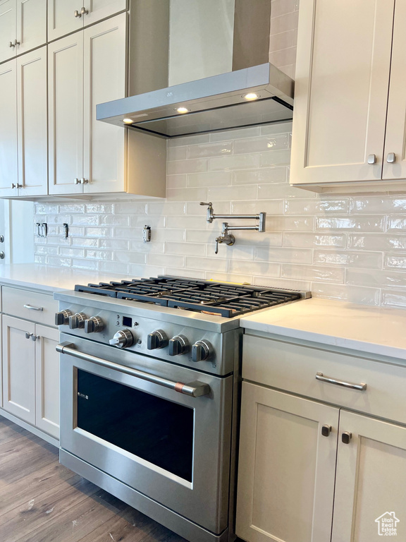 Kitchen featuring high end stainless steel range oven, wall chimney exhaust hood, light countertops, and light wood-type flooring