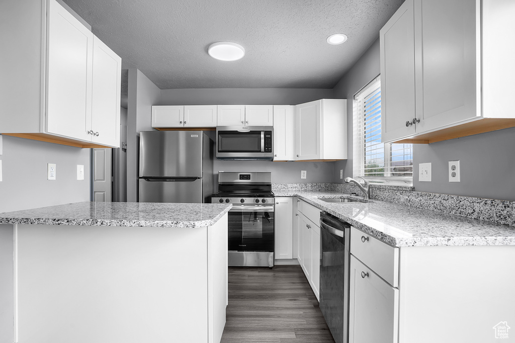 Kitchen with appliances with stainless steel finishes, a sink, a textured ceiling, white cabinetry, and light stone counters