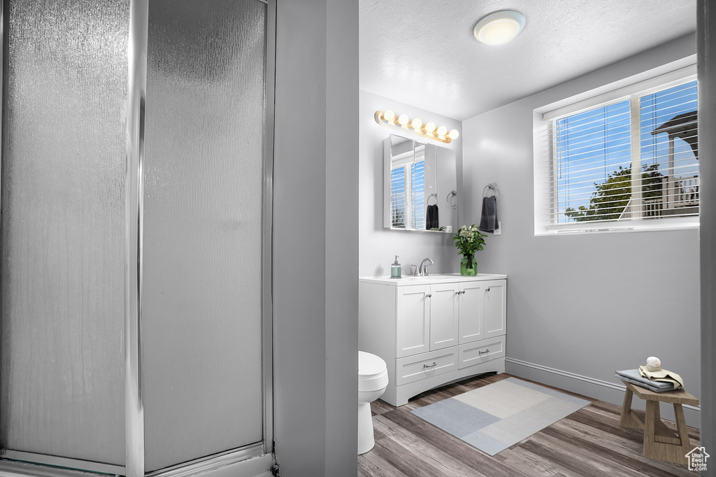 Bathroom featuring wood finished floors, a stall shower, toilet, vanity, and baseboards