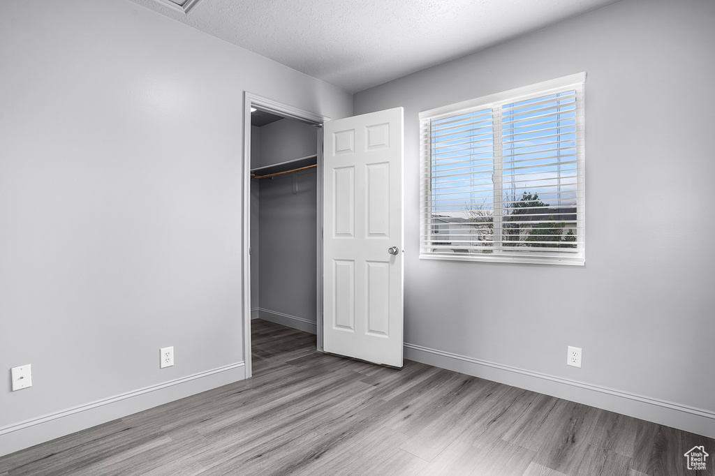 Unfurnished bedroom featuring wood finished floors, baseboards, a closet, a textured ceiling, and a walk in closet