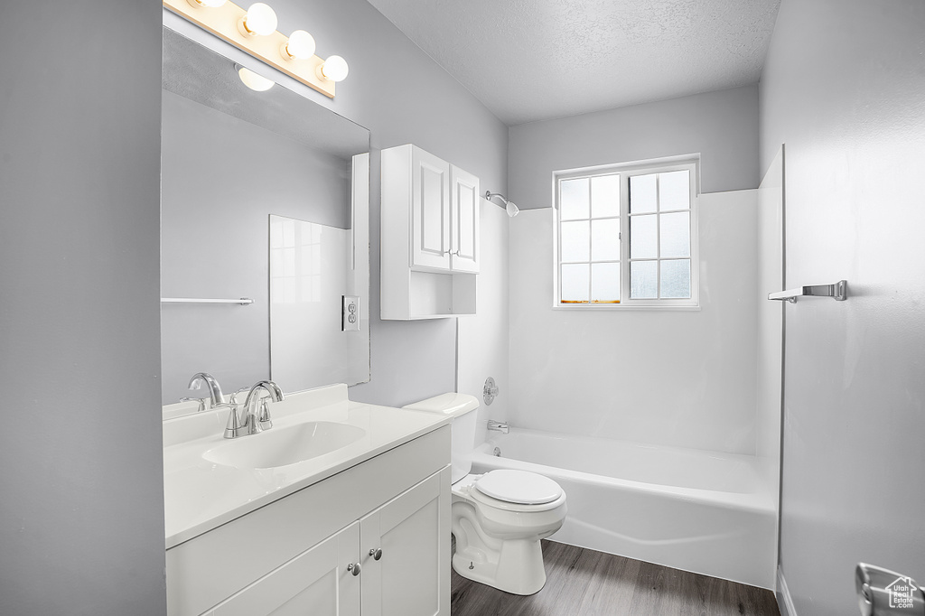 Full bath featuring wood finished floors, a textured ceiling, vanity, toilet, and bathtub / shower combination