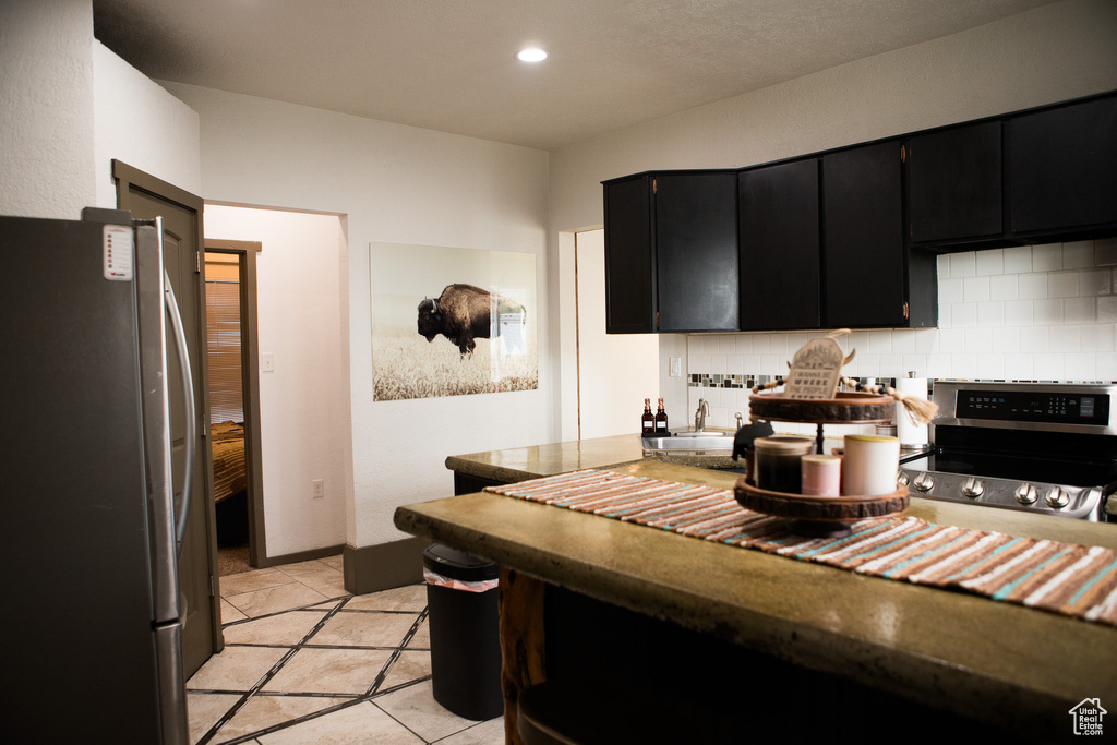Kitchen featuring appliances with stainless steel finishes, dark cabinets, decorative backsplash, light tile patterned floors, and a sink