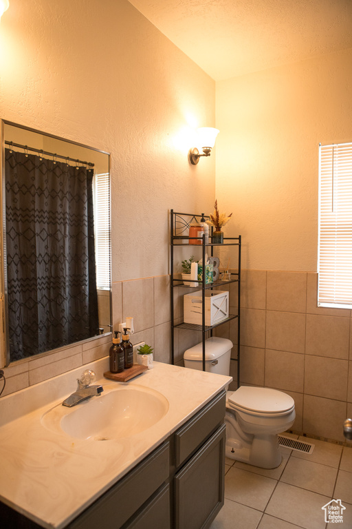 Bathroom featuring tile walls, tile patterned flooring, vanity, toilet, and a textured wall