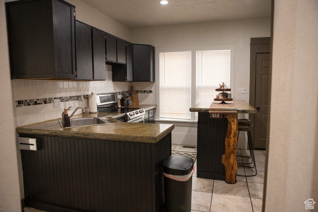 Kitchen with stainless steel range with electric cooktop, a sink, a peninsula, backsplash, and recessed lighting