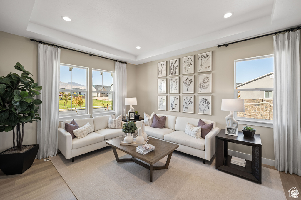 Living area featuring a raised ceiling, plenty of natural light, recessed lighting, and light wood-style flooring