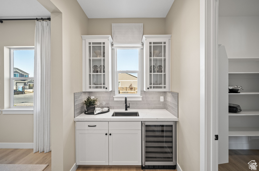 Indoor wet bar with wine cooler, wood finished floors, decorative backsplash, and healthy amount of natural light