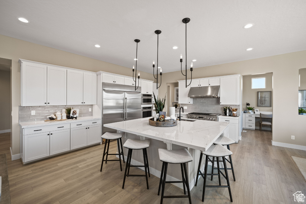 Kitchen featuring under cabinet range hood, stainless steel appliances, decorative backsplash, light wood-style flooring, and recessed lighting