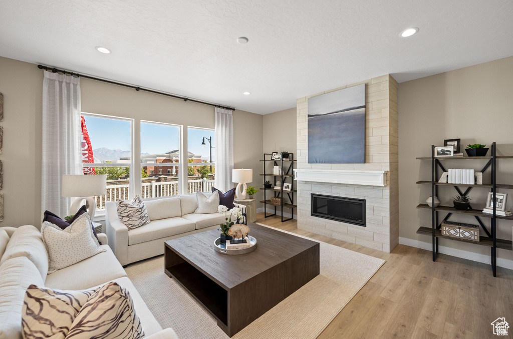 Living room with light wood-type flooring, recessed lighting, a large fireplace, and baseboards