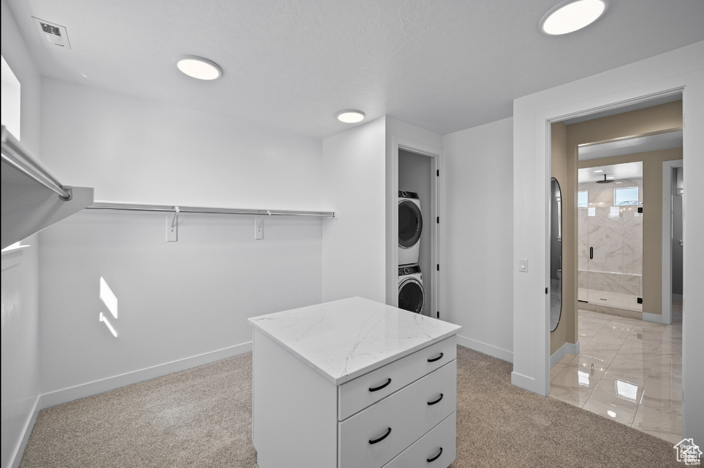 Spacious closet with stacked washing machine and dryer and light colored carpet