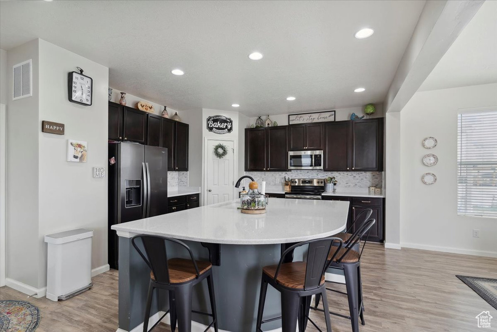 Kitchen featuring stainless steel appliances, a kitchen bar, light wood finished floors, tasteful backsplash, and light countertops