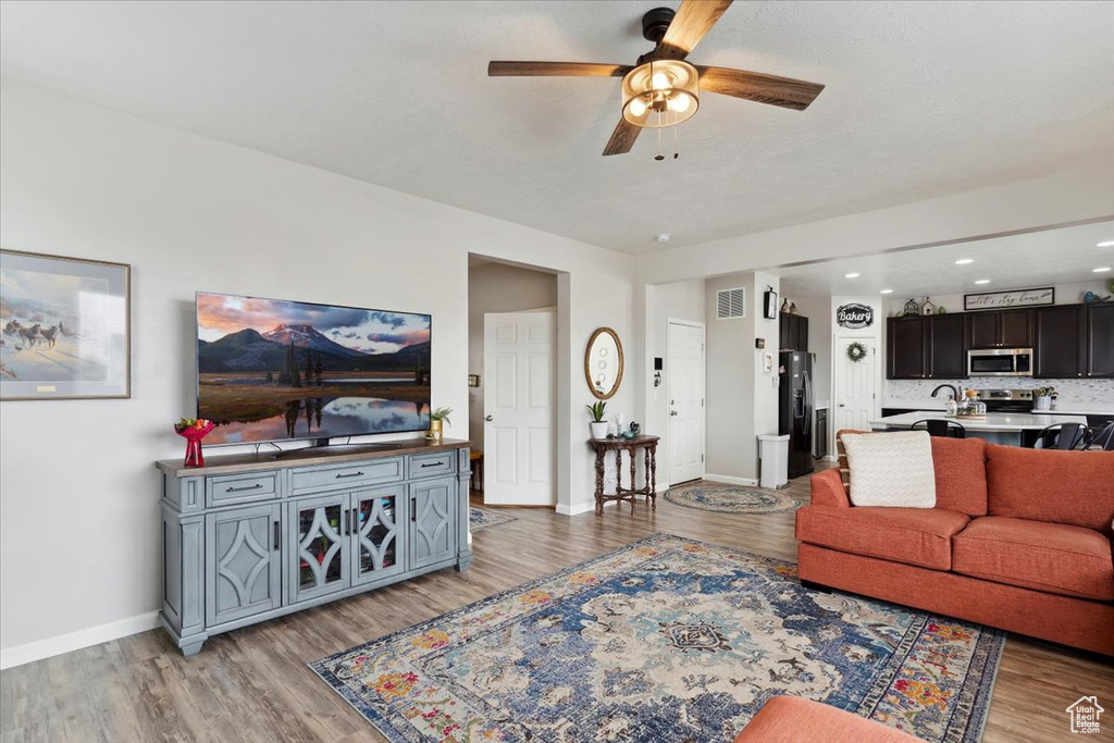 Living area with a ceiling fan, light wood-style flooring, and baseboards