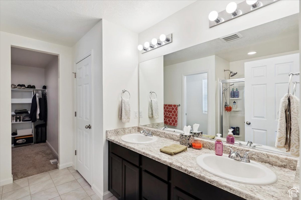 Bathroom featuring a shower stall, tile patterned flooring, double vanity, and baseboards
