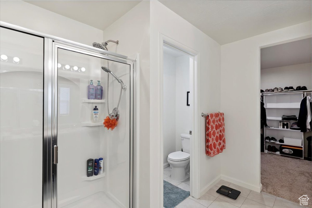 Bathroom with a stall shower, tile patterned floors, toilet, baseboards, and a spacious closet